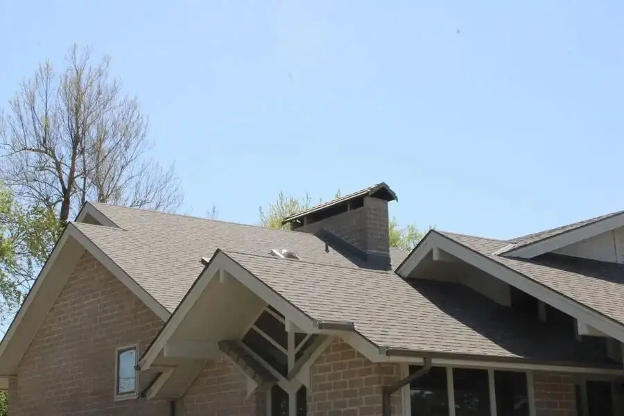 Gray shingle roof with a gabled porch and brick chimney over a tan block home