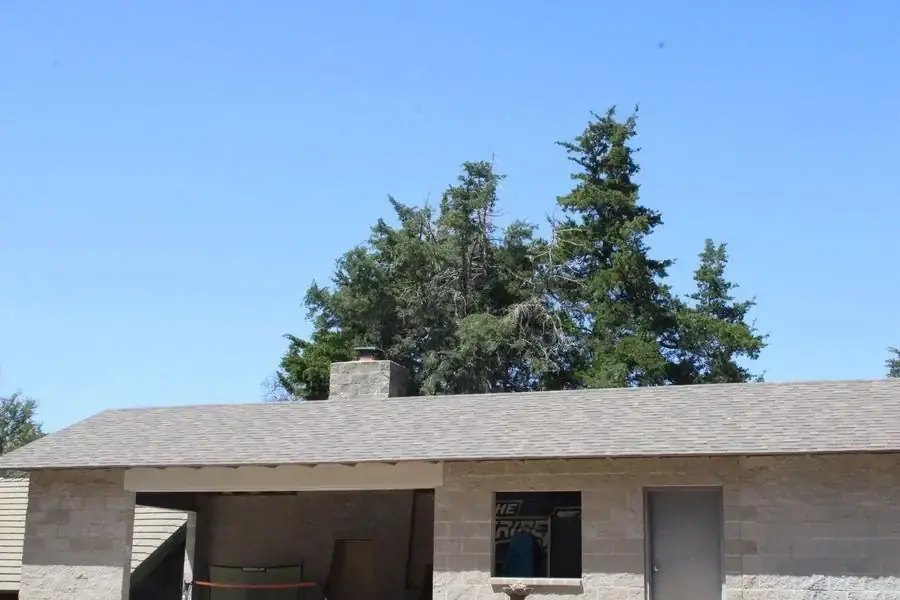 Long low-slope gray shingle roof over a block building with an open carport