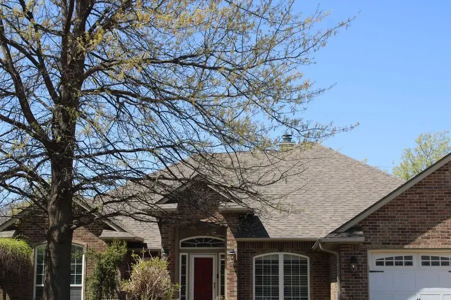 Brick two-story home with a gray shingle roof behind a large bare-branched tree