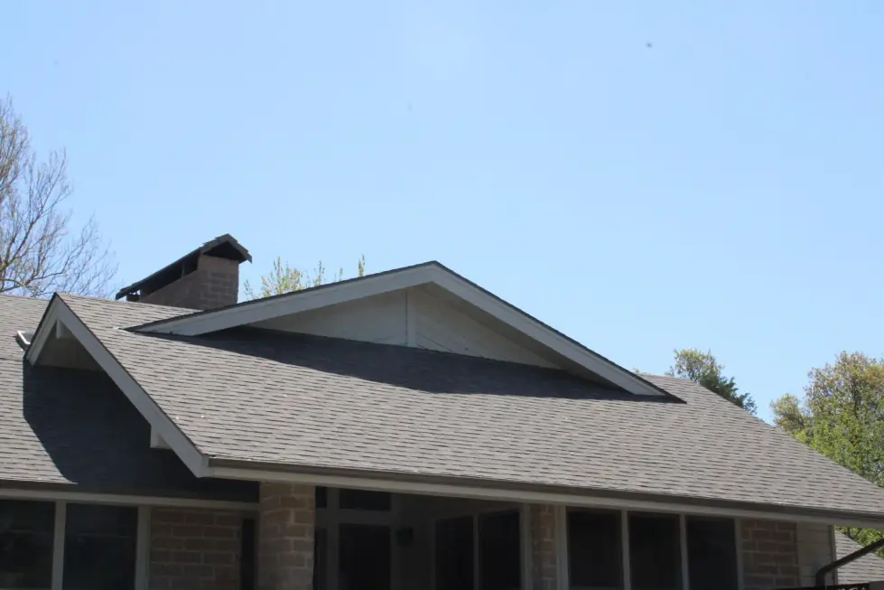 Gray shingle roof with a wide front gable over brick piers and a screened porch